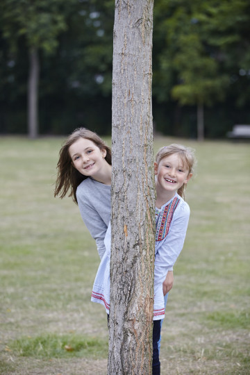 Siblings hiding behind tree trunk